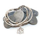 Stack of silver bracelets with a Celtic knot charm on a white background