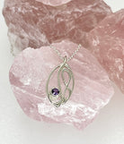 Silver pendant with a purple gemstone on a pink crystal background