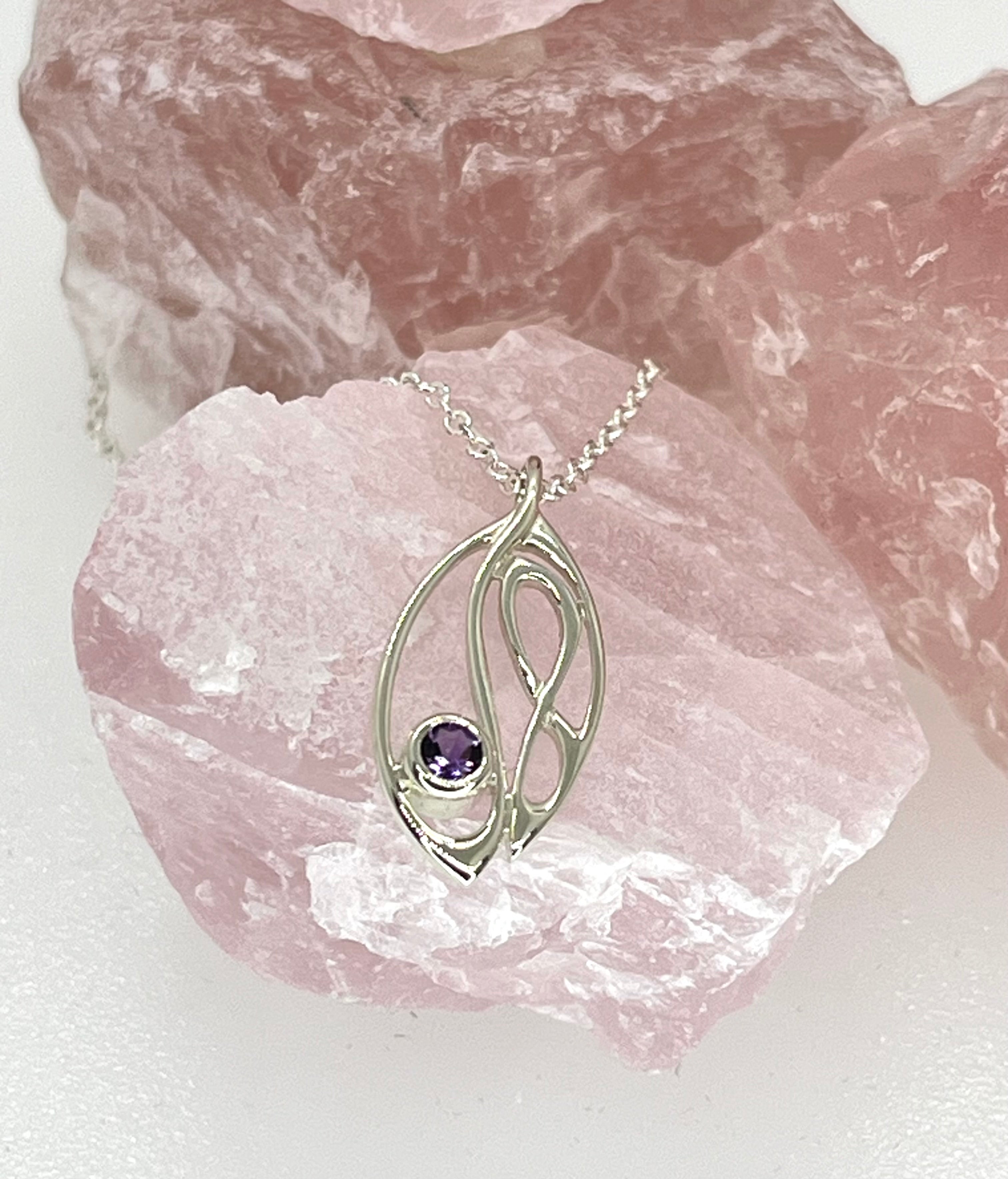 Silver pendant with a purple gemstone on a pink crystal background