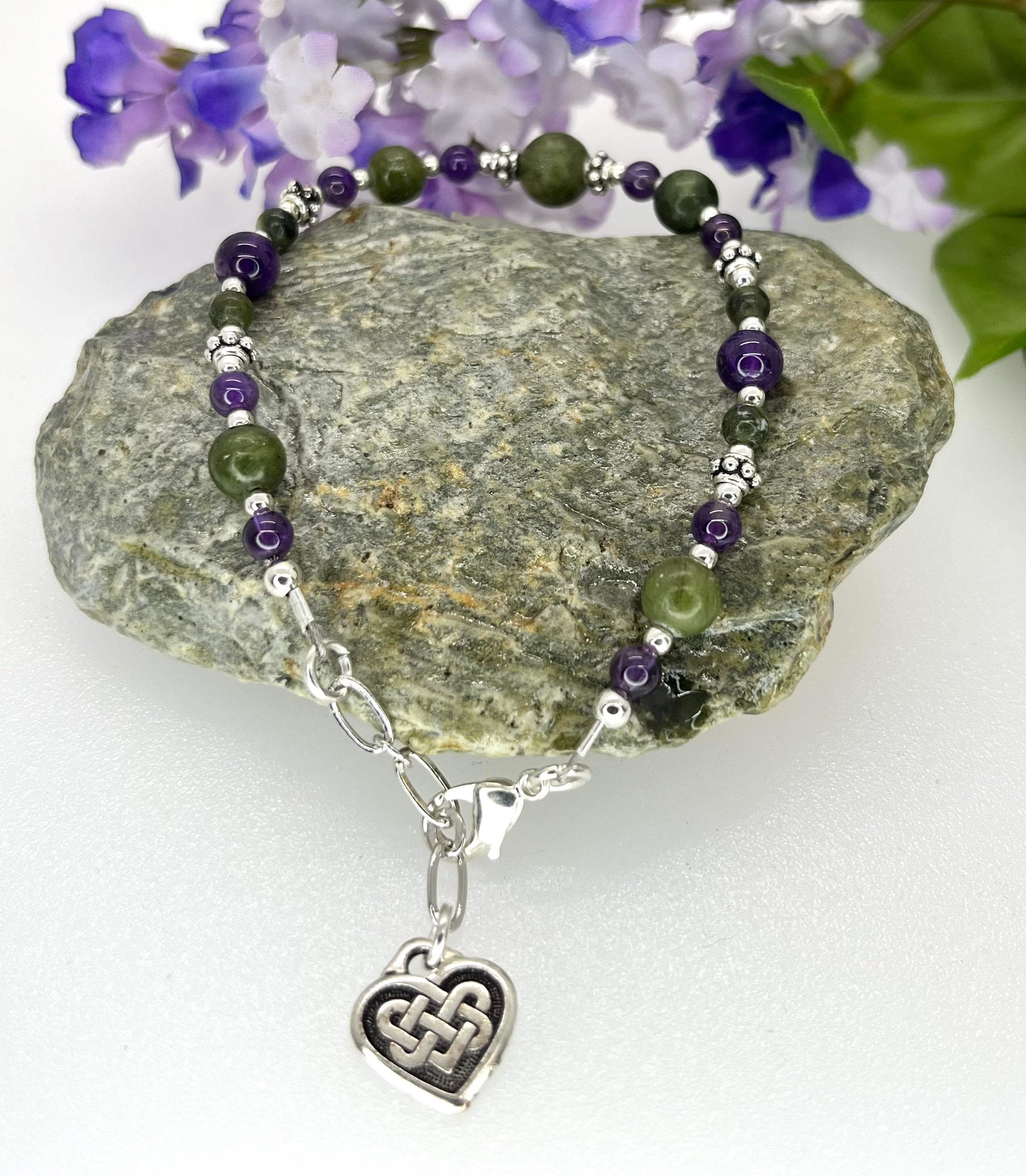 Beaded bracelet with a heart charm on a rock with flowers in the background