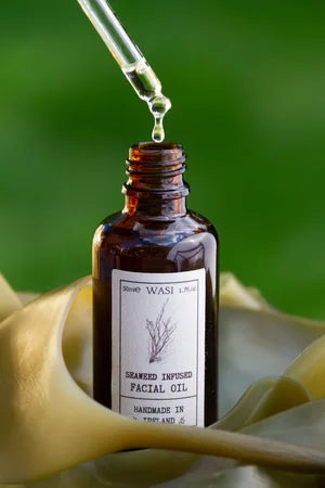 Brown glass bottle of seaweed infused facial oil with dropper on a green background