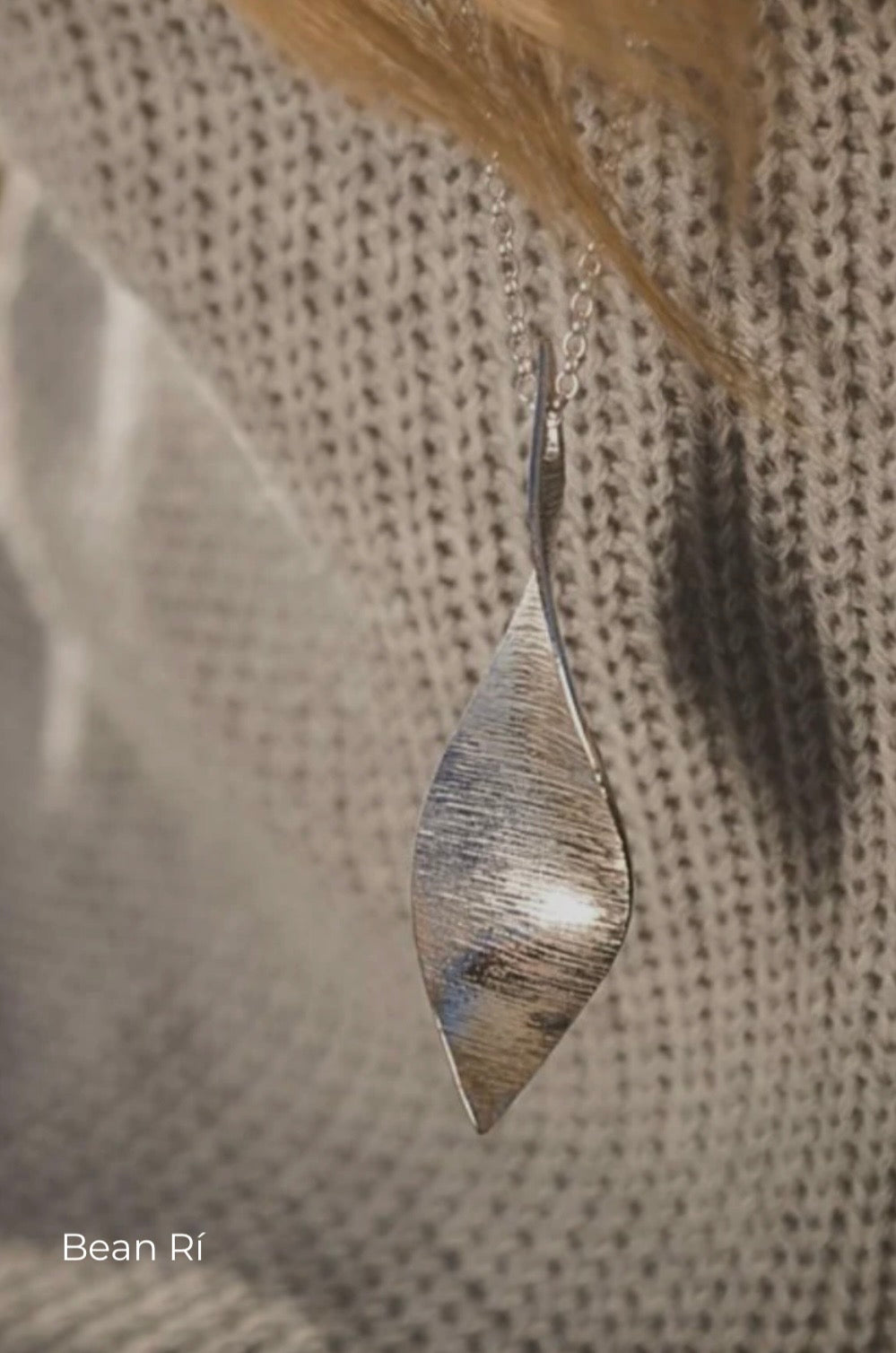 Silver pendant on a chain against a textured fabric background
