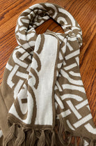 A knit scarf with a brown and off-white geometric pattern, laid flat on a wooden surface.