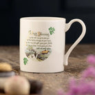White mug with an Irish blessing design on a wooden surface with flowers in the foreground