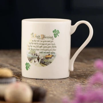 White mug with an Irish blessing design on a wooden surface with flowers in the foreground