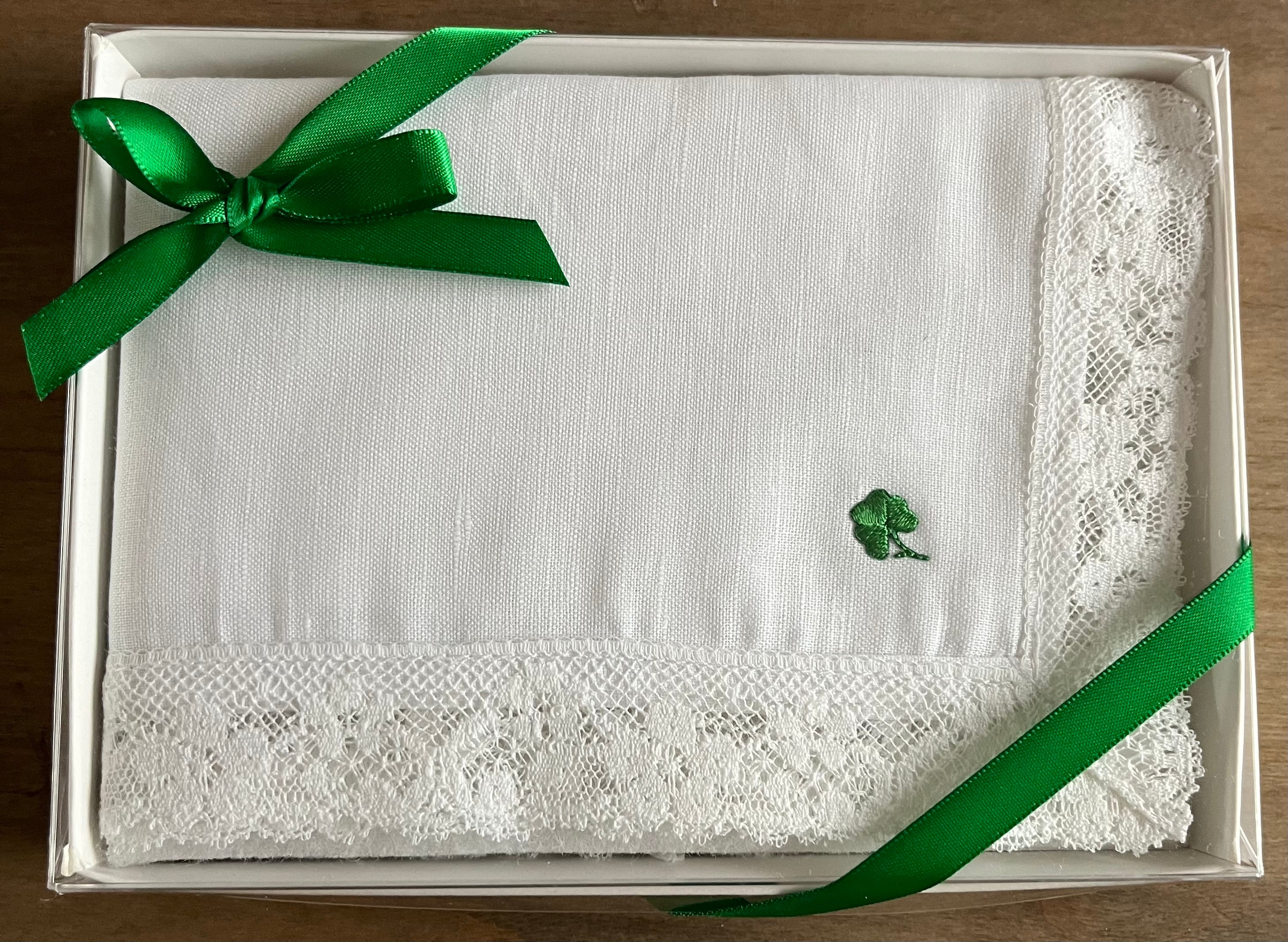 White lace handkerchief with a green shamrock  in a box on a wooden surface