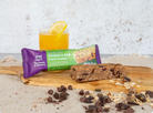 Irish Granola Bar with packaging on a wooden board with a glass of juice and scattered ingredients.