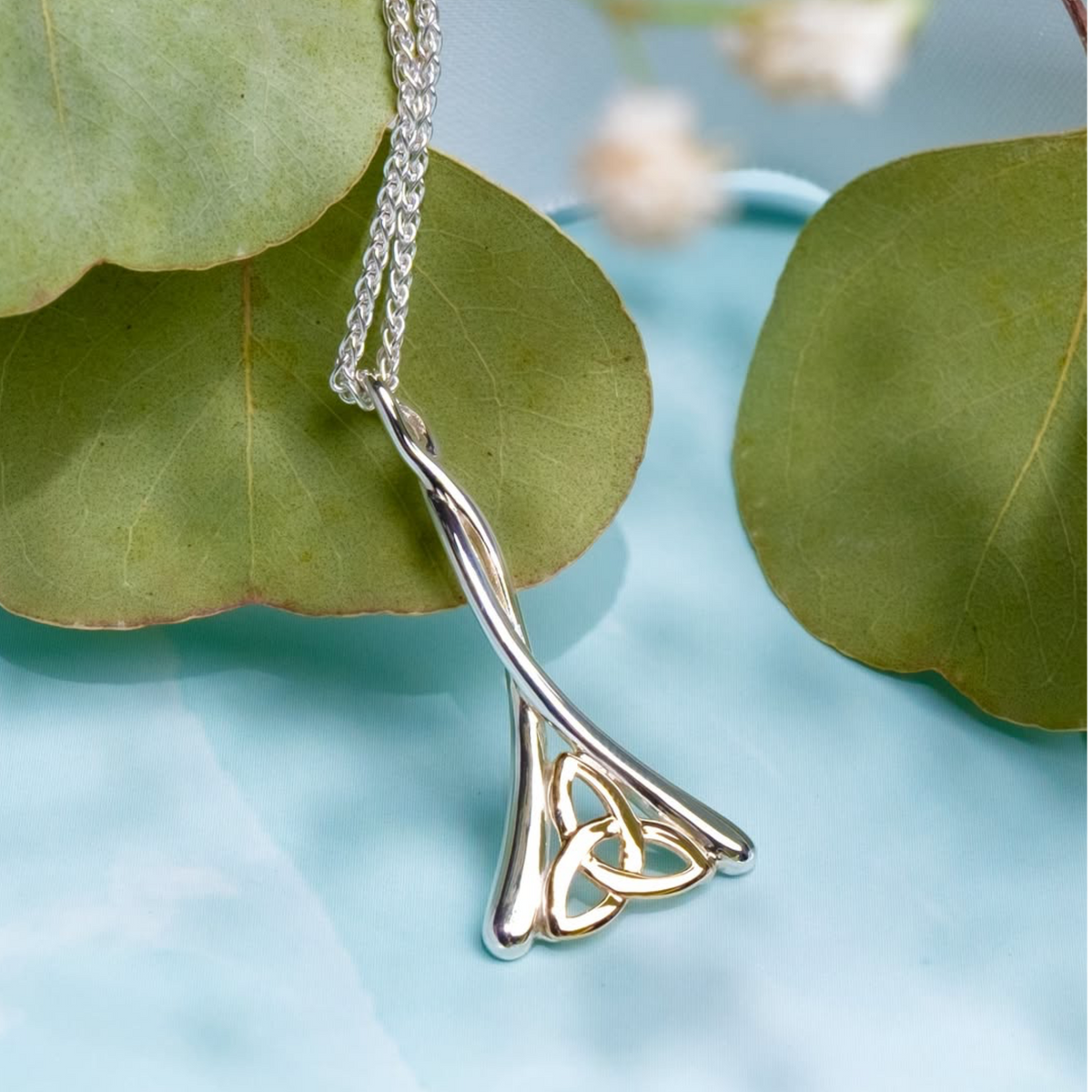 A silver Celtic knot pendant necklace with a twisted chain, styled on a light blue surface with green leaves.