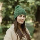 Woman wearing a green knitted hat outdoors with blurred trees in the background