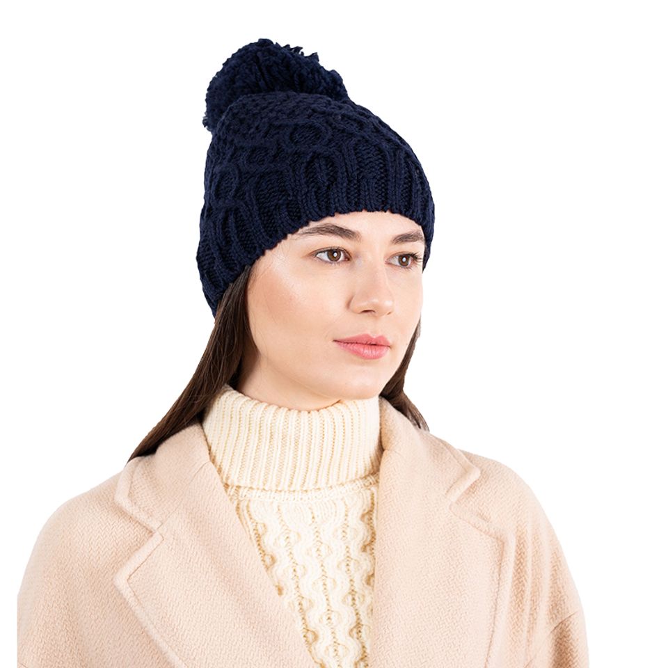 Woman wearing a navy blue knitted beanie with a pom-pom on a white background