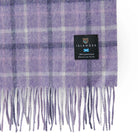 A close-up of a purple and white plaid fringed scarf with a black 'ISLANDER' brand label sewn onto one corner.