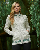 Woman wearing a cream-colored knit cardigan with green shamrock patterns against a natural background.