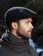 Man wearing a black flat cap and colorful scarf against a blurred natural background