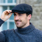Man wearing a gray wool cap and sweater, adjusting his cap against a blurred background.