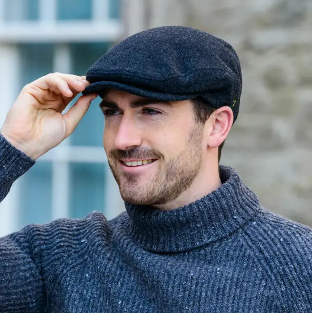 Man wearing a gray wool cap and sweater, adjusting his cap against a blurred background.