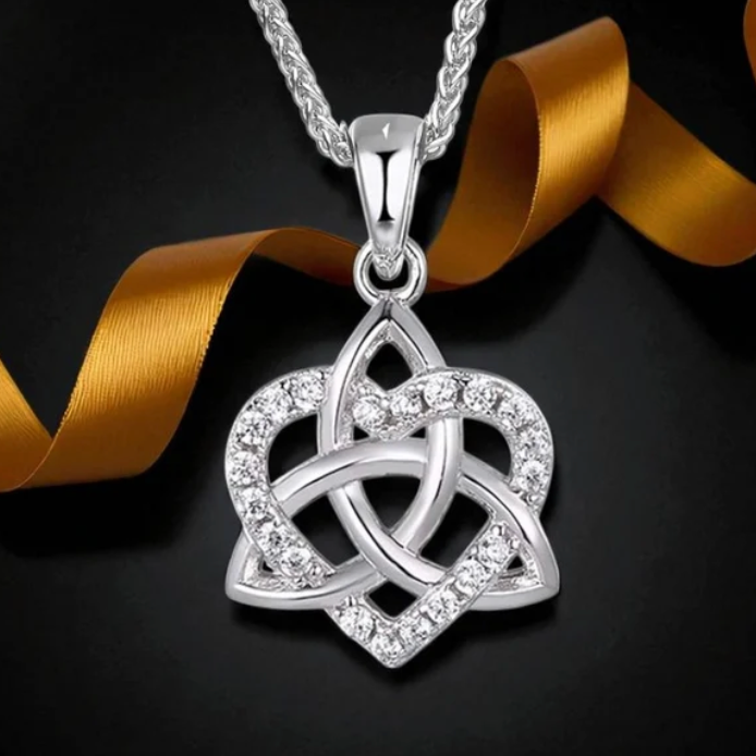 A silver Celtic knot pendant necklace with clear crystals, displayed on a black background with a gold ribbon.