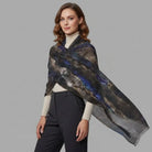 A woman modeling a lightweight shawl with an abstract cosmic pattern in black, gray, and blue, draped over her shoulders against a solid gray studio background.