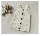 White crocheted dress with buttons on a light gray surface with decorative flowers.