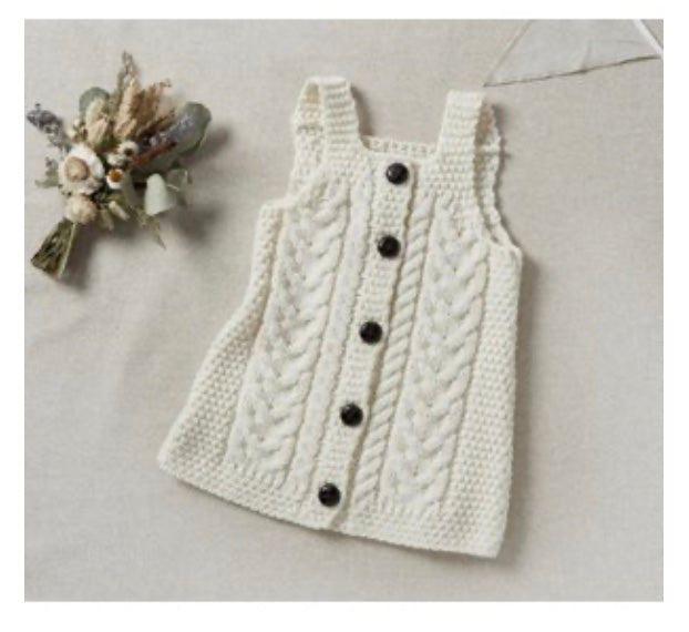 White crocheted dress with buttons on a light gray surface with decorative flowers.