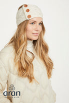 Woman wearing a cream-colored knit headband with buttons and a matching coat on a white background, featuring the Aran Woolen Mills logo.