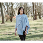 A woman wearing a light blue wrap poncho with a knotted front detail, standing in a park with trees and grass in the background.