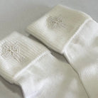 White baby socks with Celtic cross design on a light gray background
