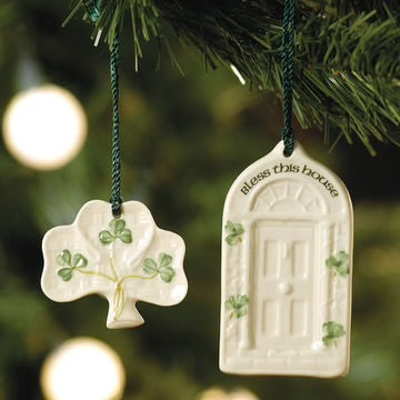 Two ceramic Christmas ornaments hanging on a tree with blurred lights in the background.
