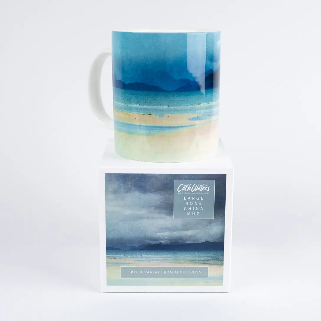 A ceramic mug with an abstract beach landscape print in shades of blue, teal, and beige, displayed on top of its branded retail box against a clean white background.