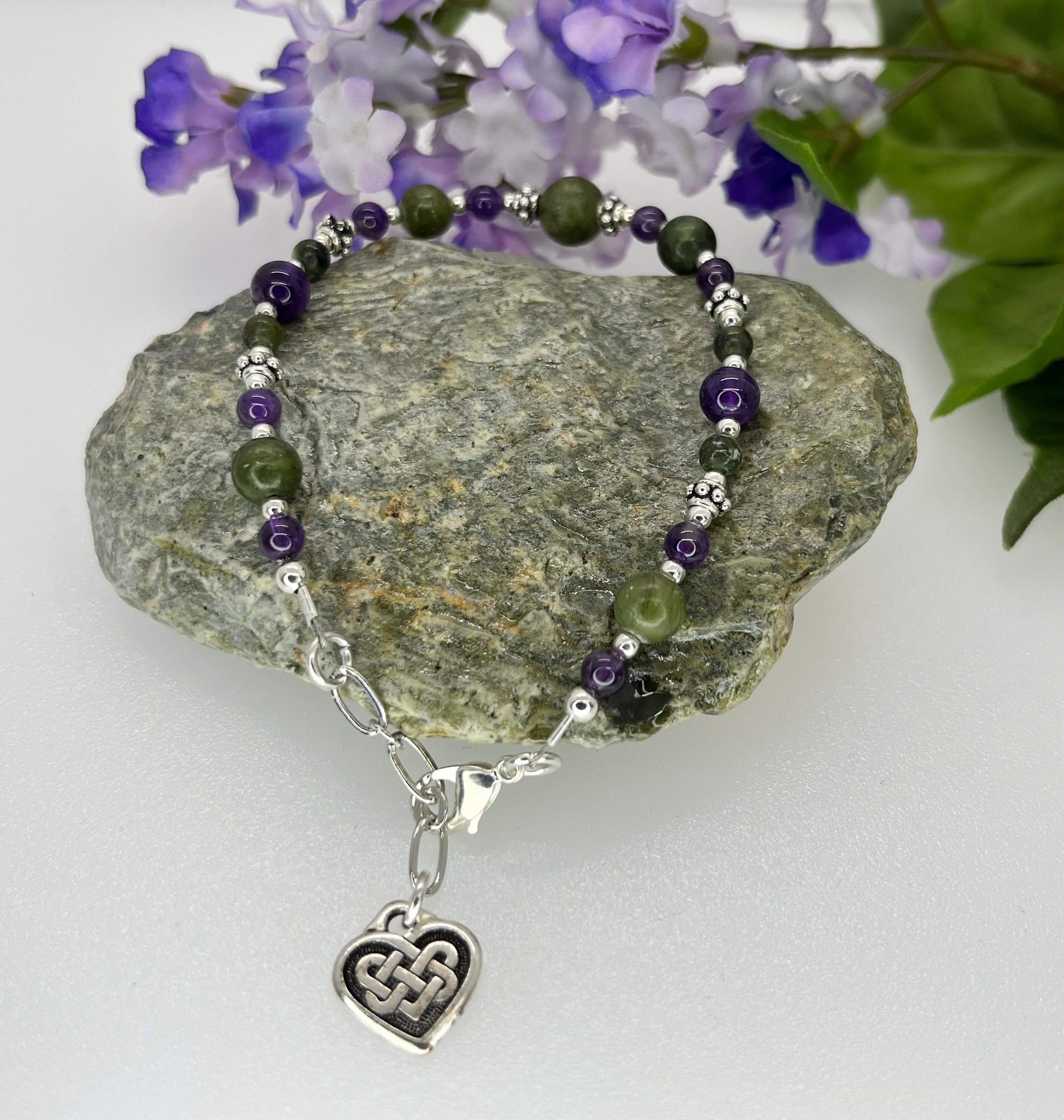 Beaded bracelet with a heart charm on a rock with flowers in the background