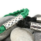 Bracelet with green and black braided cord and silver Celtic knot design on stones.