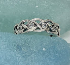 Silver ring with braided design and embedded diamonds on a light blue background