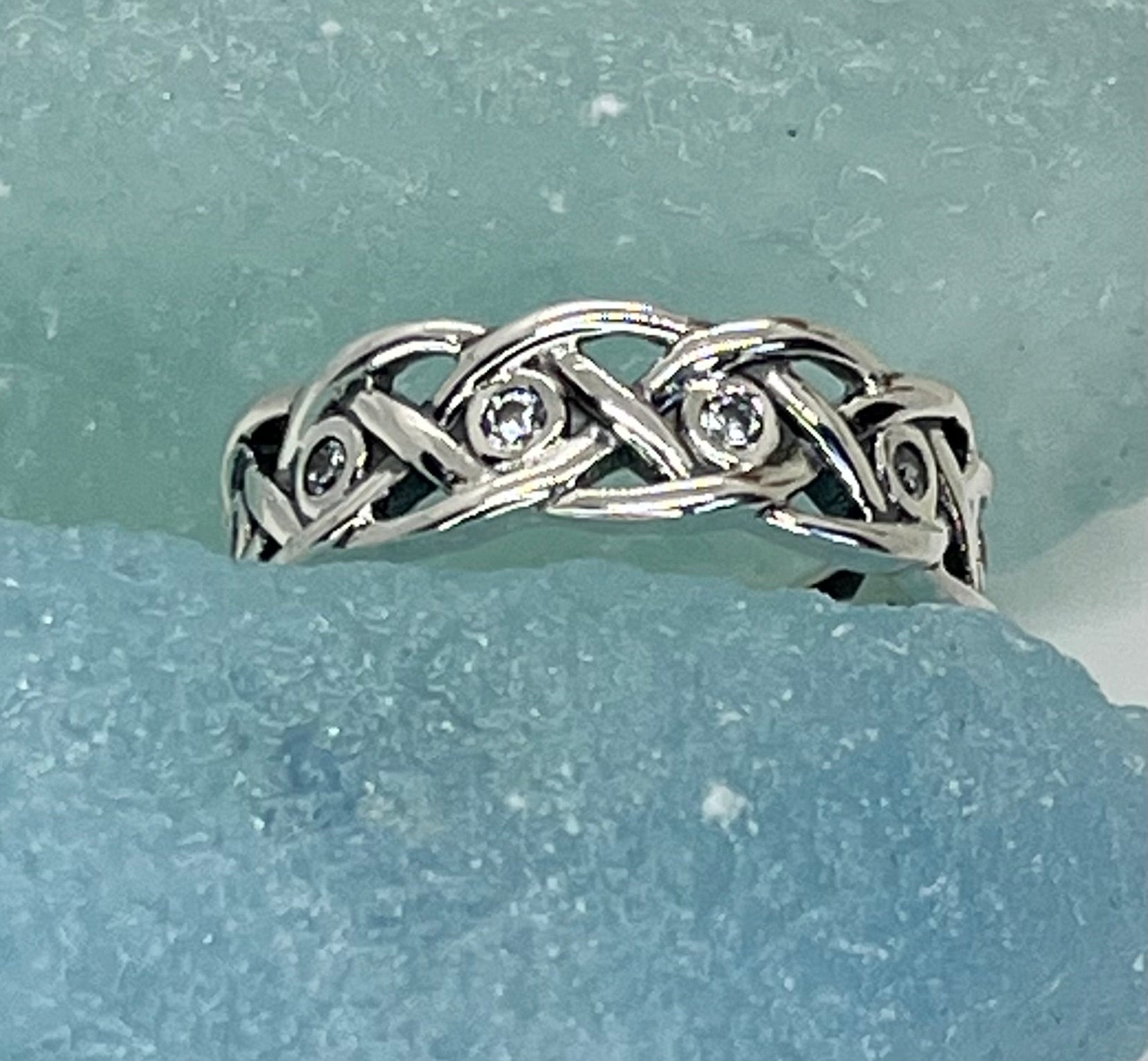 Silver ring with braided design and embedded diamonds on a light blue background
