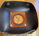 Brown leather tray with a shamrock design on a black leather surface