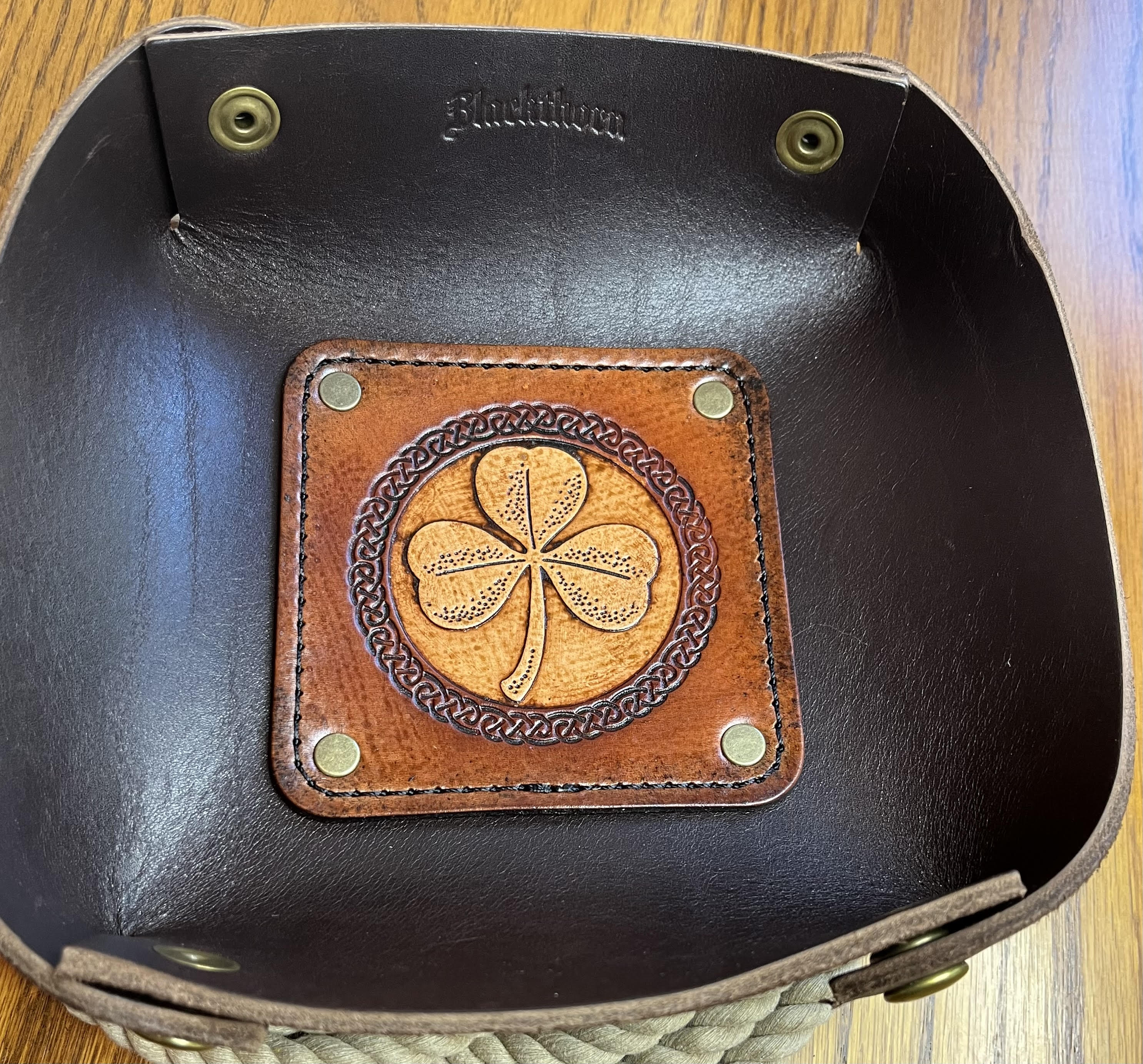 Brown leather tray with a shamrock design on a black leather surface