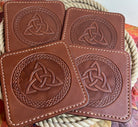 Four brown leather coasters with Celtic knot design on a woven surface.