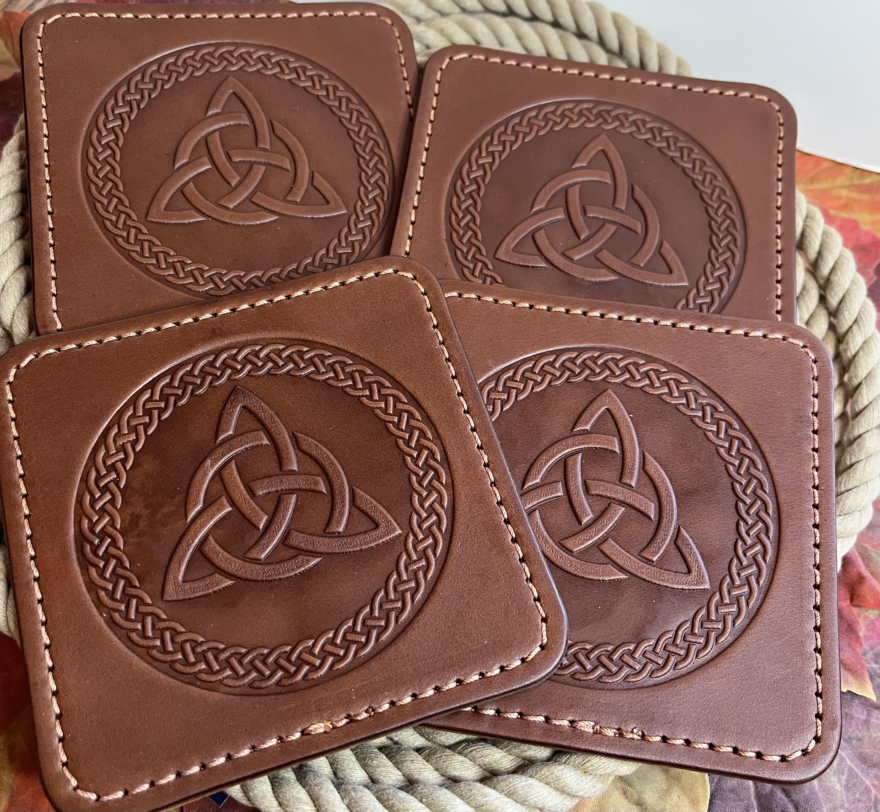 Four brown leather coasters with Celtic knot design on a woven surface.