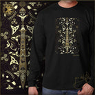 Black long-sleeve shirt with gold and white intricate design called celtic warrior worn by a person, with a decorative background.