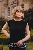 Woman wearing a black sleeveless top with a patterned hem in front of a building.