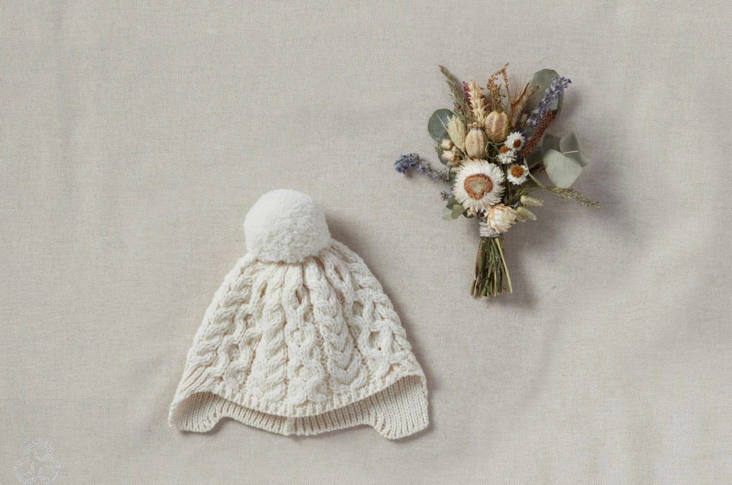 Knitted baby hat with a pom-pom and a small bouquet of flowers on a neutral background
