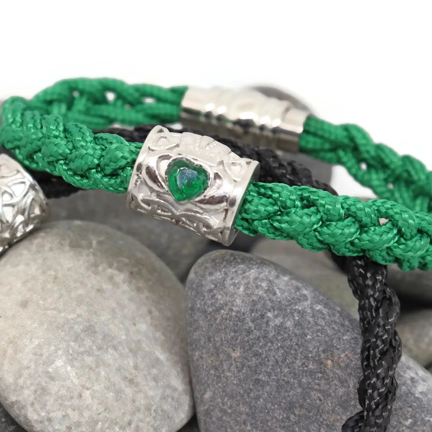 Green braided bracelet with silver clasp on pebbles