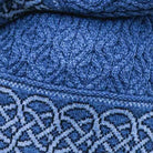 Close-up of a blue knitted textile with a textured cable-knit pattern and a contrasting light blue and navy woven border.