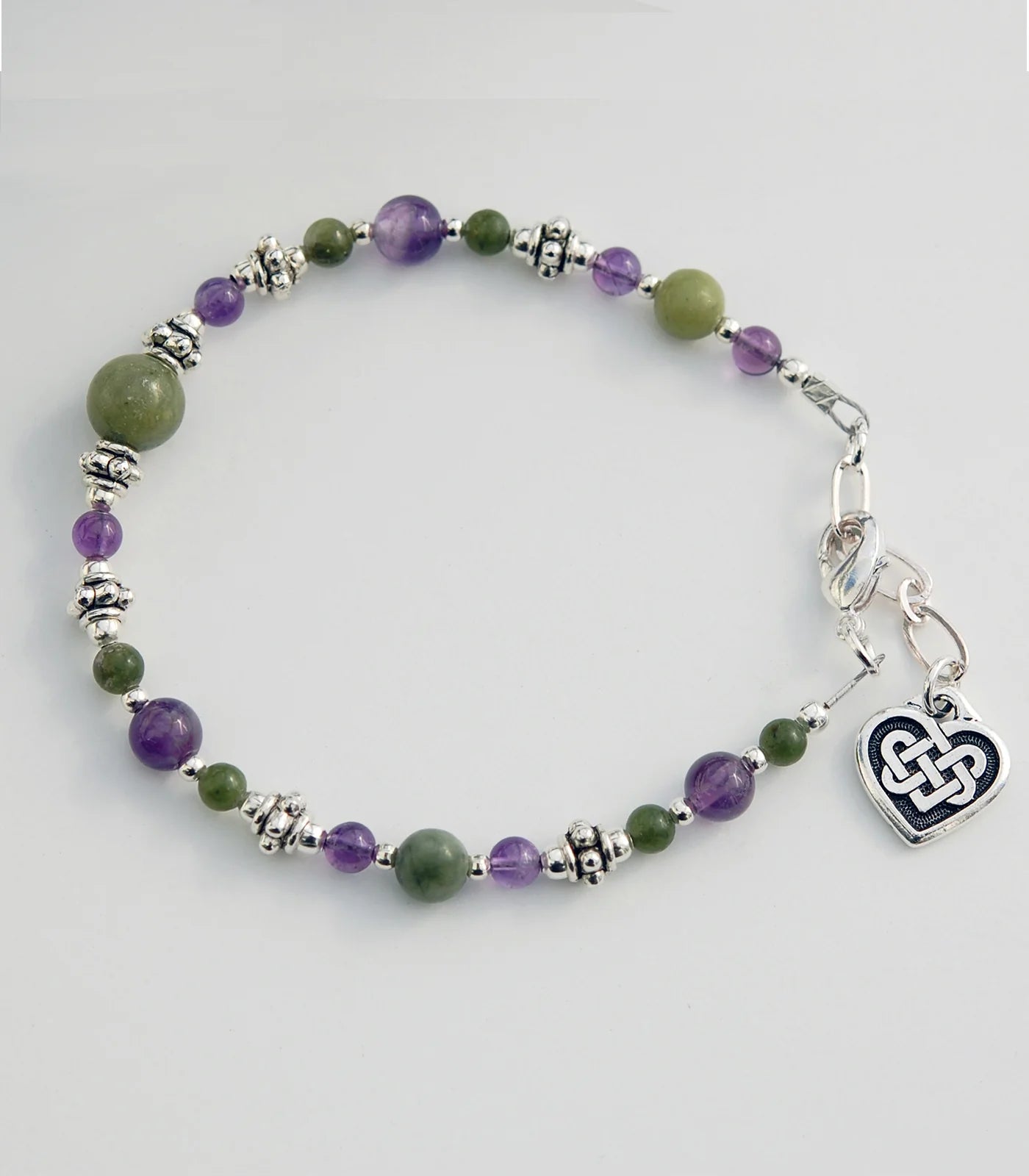 Beaded bracelet with a Celtic heart charm on a light gray background