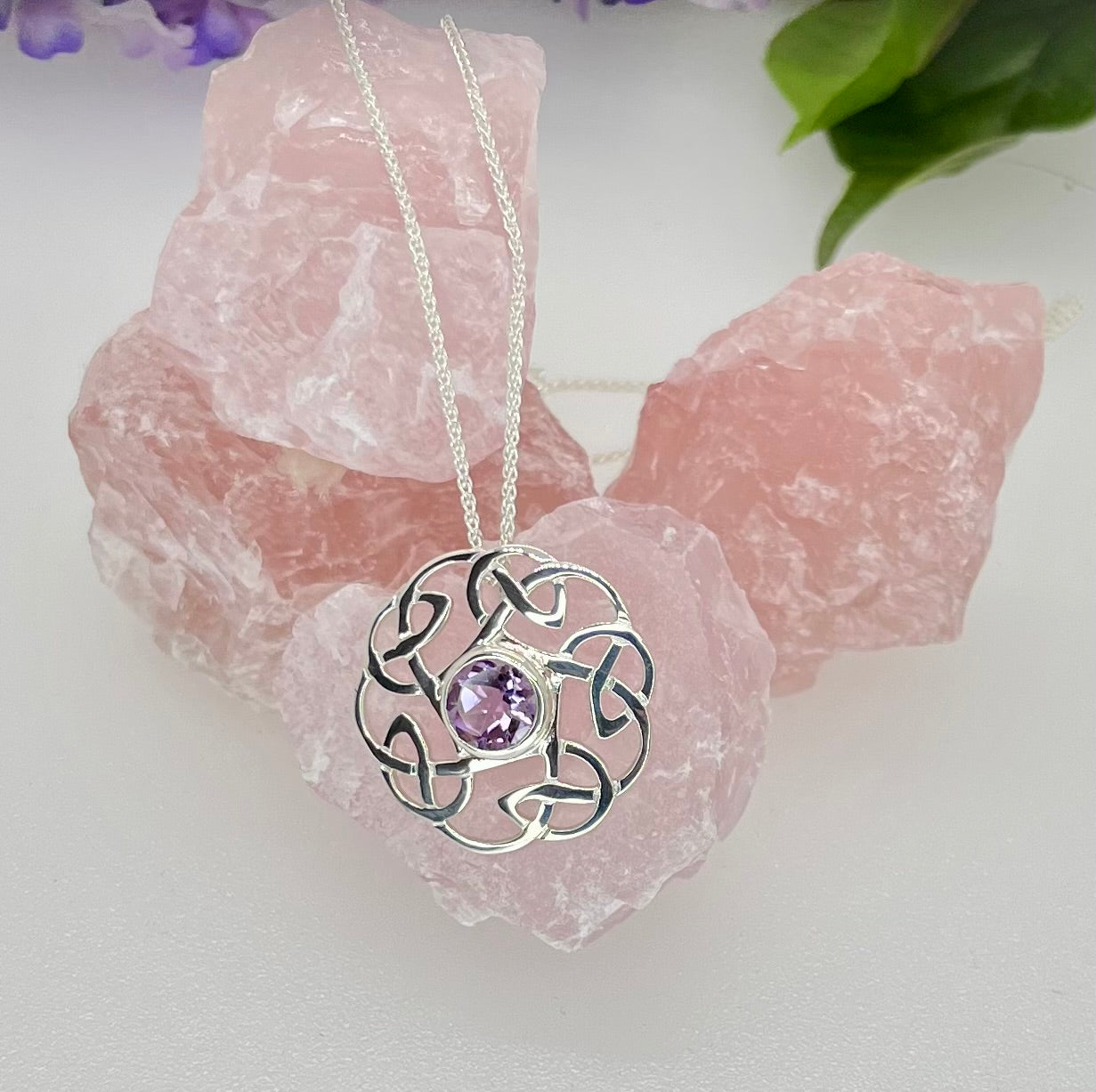 Silver necklace with a purple gemstone pendant on a pink crystal background