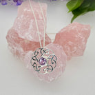 Silver necklace with a purple gemstone pendant on a pink crystal background