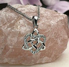 A silver Celtic knot triquetra pendant necklace with clear stones, resting on a pink rose quartz crystal.