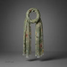 A lightweight scarf in sage green with a delicate floral pattern, draped in a loop to show its length and pattern, set against a dark gray studio background.