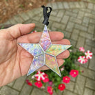 Hand holding a star-shaped iridescent ornament with flowers and pavement in the background