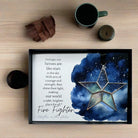 Framed artwork with star design and text on a wooden surface with coffee and mug.
