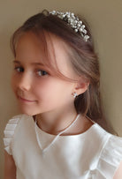 Young girl wearing a pearl tiara and necklace against a plain background