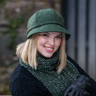 Woman wearing a green hat and scarf, smiling outdoors.